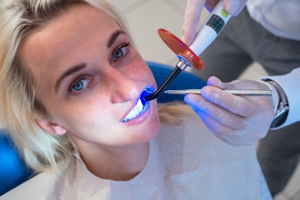 Dentist using dental curing UV lamp on teeth of patient.